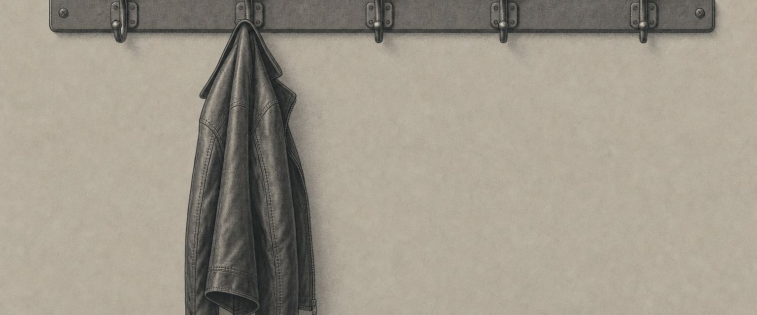 Eine Hakenleiste mit fünf Haken an einer Wand, nur am zweiten Haken hängt eine Lederjacke